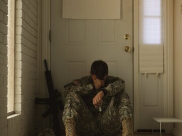 A solitary soldier in uniform sitting by a door, reflecting mood.