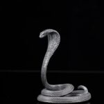 Elevated metal cobra figurine on a glossy black surface with a reflective effect.
