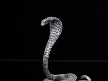 Elevated metal cobra figurine on a glossy black surface with a reflective effect.