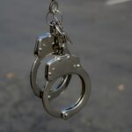 Close-up of metallic handcuffs with keys hanging outdoors, symbolizing security and law enforcement.
