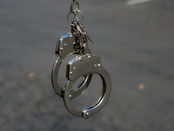 Close-up of metallic handcuffs with keys hanging outdoors, symbolizing security and law enforcement.