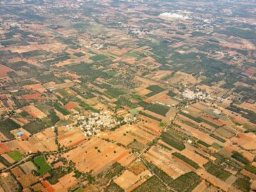 Aerial view of diverse agricultural landscape featuring cropland, villages, and greenery under daylight.