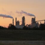 Factory chimneys releasing smoke during a vibrant sunset, highlighting industrial pollution.
