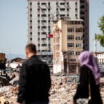 People walking past damaged buildings in Malatya, Turkey, highlighting urban earthquake destruction.