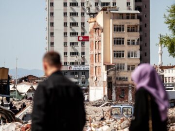 People walking past damaged buildings in Malatya, Turkey, highlighting urban earthquake destruction.
