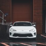 A white sports car parked in a rainy urban area, emphasizing its sleek design.