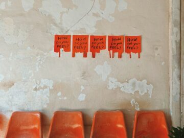 A row of empty, worn orange seats against a shabby wall with posters reading 'How Do You Feel?' in Chiang Mai, Thailand.