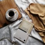 An aesthetically pleasing still life featuring a coffee cup, book, and draped fabric.
