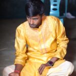 A man in a yellow kurta sits cross-legged indoors, engaging in a traditional ritual.