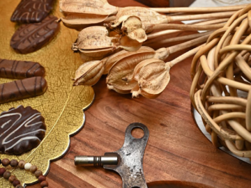 An artistic still life featuring chocolate confections, a vintage key, and rustic decor elements on a wooden board.