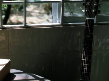 Guitar leaning against a window, casting shadows on a table in a dimly lit room.