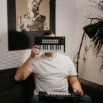 A man sitting on a couch indoors, holding a keyboard controller over his face, creating a playful scene.