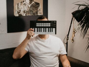 A man sitting on a couch indoors, holding a keyboard controller over his face, creating a playful scene.