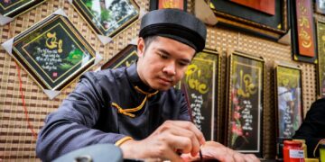 An artist in traditional attire creates beautiful Vietnamese calligraphy indoors.