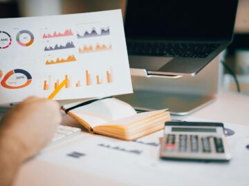 Close-up of hands analyzing financial data with charts, laptop, and calculator.