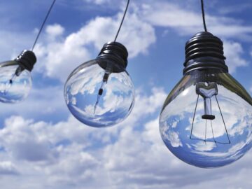Surreal image of light bulbs reflecting blue sky and clouds, symbolizing creativity and energy.