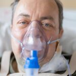 Close-up of a man in a hospital bed wearing an oxygen mask, highlighting healthcare needs.