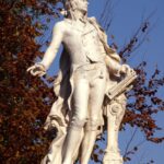Sculpture of Mozart in a serene autumn setting with vibrant leaves.