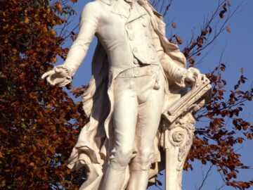 Sculpture of Mozart in a serene autumn setting with vibrant leaves.