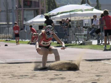 Female athlete captured mid-landing in the long jump event during a sunny sports meet.