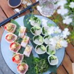 Top view of a sushi platter featuring sashimi rolls, avocado, and greens on a wooden table.