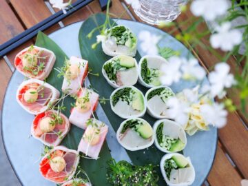 Top view of a sushi platter featuring sashimi rolls, avocado, and greens on a wooden table.