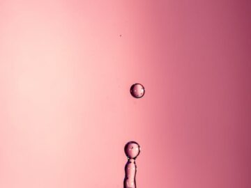 A mesmerizing shot of a water droplet captured mid-air against a pink backdrop, showcasing dynamic motion.