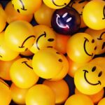A vibrant collection of yellow smiley face balloons with one unique dark balloon.
