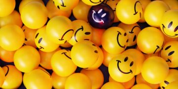 A vibrant collection of yellow smiley face balloons with one unique dark balloon.