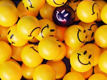 A vibrant collection of yellow smiley face balloons with one unique dark balloon.
