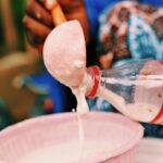 A person pouring fresh, homemade yogurt from a plastic bottle into a pink bowl, illustrating traditional food preparation.