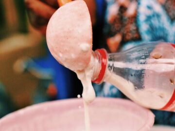 A person pouring fresh, homemade yogurt from a plastic bottle into a pink bowl, illustrating traditional food preparation.