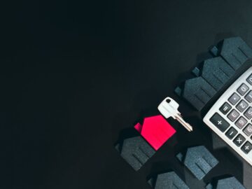 Real estate concept image featuring a calculator, houses, and a key on a black background.