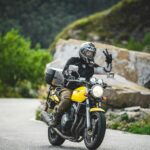 A motorcyclist rides through a scenic mountain road, making a peace sign.