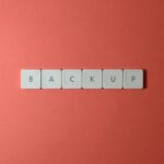 Close-up of keyboard keys spelling 'BACKUP' placed on a coral-colored surface.