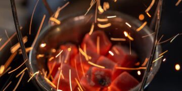 Close-up of glowing red coals with flying sparks in a metal basket, dramatic and dynamic.