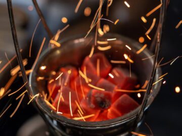 Close-up of glowing red coals with flying sparks in a metal basket, dramatic and dynamic.