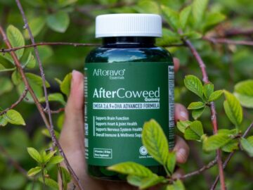 Hand holding a supplement bottle amidst vibrant green foliage outdoors.