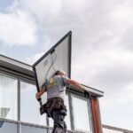 A worker installs a solar panel on a residential rooftop emphasizing renewable energy.
