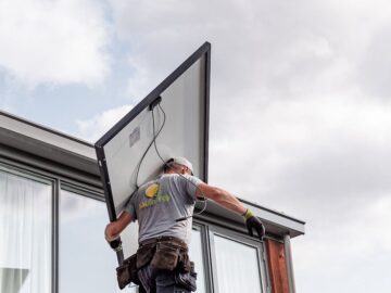 A worker installs a solar panel on a residential rooftop emphasizing renewable energy.