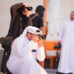 Group of photographers in Doha capturing cityscapes, embracing cultural attire and modern technology.