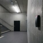 Minimalist concrete staircase with security device in office building corridor.