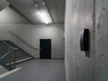 Minimalist concrete staircase with security device in office building corridor.