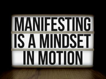 Inspirational quote 'Manifesting is a mindset in motion' on lightbox over dark background.