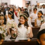 Young girls in white dresses participate in a beautiful First Communion ceremony at a church.