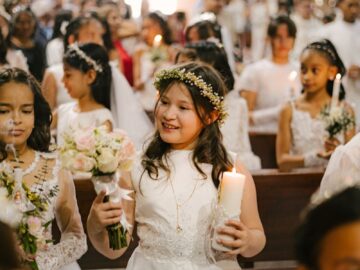Young girls in white dresses participate in a beautiful First Communion ceremony at a church.
