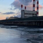 A serene view of an industrial power plant with smokestacks releasing vapor against a sunset sky.