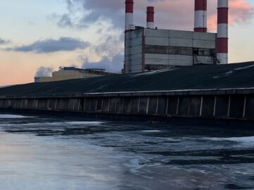 A serene view of an industrial power plant with smokestacks releasing vapor against a sunset sky.