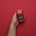 Close-up of a hand holding a red deodorant stick against a red background.