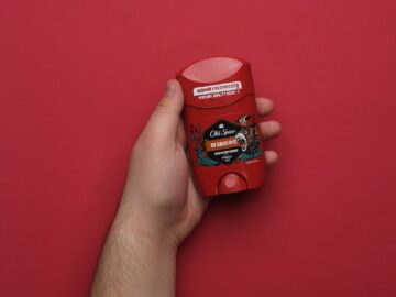 Close-up of a hand holding a red deodorant stick against a red background.